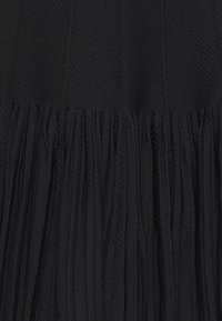 Tissu noir plissé avec une texture côtelée verticale, présentant des fines lignes et un drapé souple, créant un aspect fluide à l’ourlet.