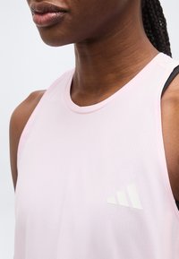 Gros plan sur une personne portant un haut de sport sans manches rose clair avec un petit logo blanc Adidas sur la poitrine.