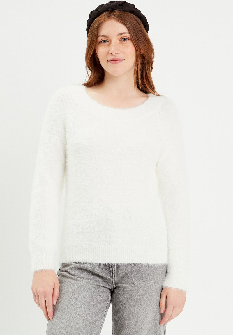 Pull en laine blanc duveteux avec un col rond et des manches longues, fabriqué à partir d'un matériau texturé doux. Associé à un jean gris.