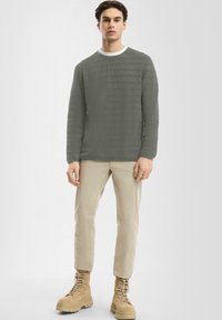 Szary sweter prążkowany z okrągłym dekoltem, połączony z beżowymi spodniami slim-fit i brązowymi sznurowanymi butami. Gładka faktura w całej stylizacji.