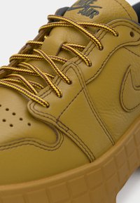 Gros plan d'une basket en cuir jaune moutarde avec des lacets ronds bordeaux et jaunes, des coutures détaillées et une semelle en caoutchouc épaisse.