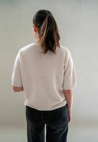 Pull en maille crème à manches courtes, coupe ample, porté sur un jean foncé. Texture lisse avec des détails subtils sur le tissu.
