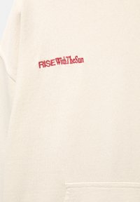 Felpa beige con una texture morbida, con il testo ricamato in rosso "RISE With The Sun" sul lato sinistro del petto. Design semplice senza motivi.