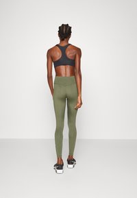 Sujetador deportivo negro, leggings de talle alto verde olivo y zapatillas deportivas negras. El material parece suave y elástico; el diseño ajustado resalta la forma.