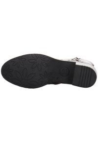 Suela de zapato de goma negra con detalles de un patrón floral, superficie texturizada y un pequeño tacón. La marca metálica es visible cerca del área del tacón.