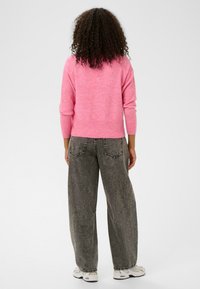 Pietais rozā džemperis ar garām piedurknēm, ribotām aprocēm un apakšmalu; apvienots ar brīviem pelēkiem džinsiem, kas aprīkoti ar aizmugurējiem kabatām un teksturētu virsmu.