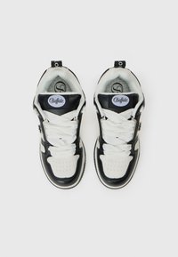 Par crnih i bijelih Buffalo tenisica s debelim bijelim vezicama, snimljenih odozgo na bijeloj pozadini.