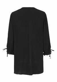 Sort langærmet bluse i tekstureret stof, løs pasform og sammenfoldede manchetter, der er bundet med små sløjfer, set fra ryggen.