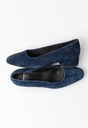 Ballerine in camoscio blu navy con punta arrotondata, tacco basso quadrato e una morbida fodera interna nera. Design minimalista senza accentuazioni visibili.