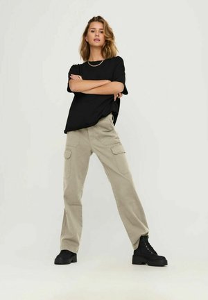 T-shirt nera in cotone, vestibilità rilassata, maniche corte. Pantaloni cargo beige, a gamba larga, con tasche laterali. Stivaletti neri con lacci e suola spessa.