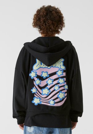 Schwarzer Kapuzenpullover mit einem großen, bunten Blumenmotiv auf dem Rücken, das pinke, blaue und grüne Blumen mit geschwungenen Linien zeigt. Weicher Stoff.