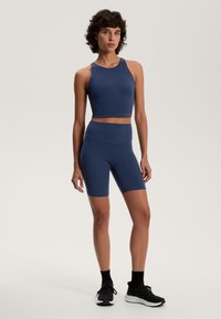 Sötétkék sport crop top és hozzáillő, magas derekú rövidnadrág rugalmas anyagból. Az öltözet elegáns, testhezálló formát mutat.