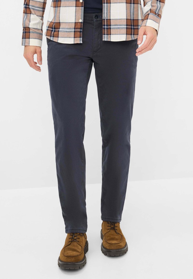 Pantaloni in cotone misto blu navy con taglio dritto, caratterizzati da una leggera texture e una cintura con chiusura a bottone, abbinati a scarpe in suede marroni.