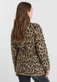 Cardigan de patrón de leopardo en beige y negro, con cinturón, mangas largas y una textura suave. Diseño de frente abierto.
