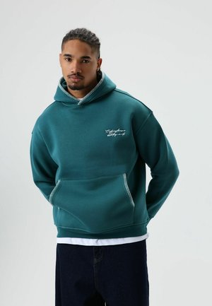 Turquoise capuchontrui met een kangoeroezak, contrasterende stiksels op de capuchon en zak, en kleine witte tekst op de borst.