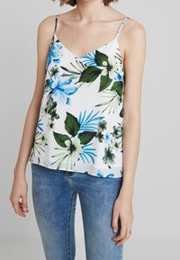 Blommig linne i lättviktig vit tyg, med blåa och gröna tropiska mönster, med V-ringning och tunna justerbara remmar.