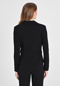 Schwarze, taillierte Blazerjacke mit einer figurschmeichelnden Silhouette, Reverskragen und langen Ärmeln. Glattes Material mit minimalen Nähdetails auf der Rückseite.