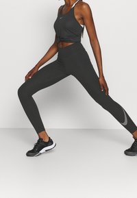 Canottiera atletica nera con il davanti annodato, abbinata a leggings neri a vita alta con un motivo a pois argentei sulla parte bassa della gamba. Sneakers nere.