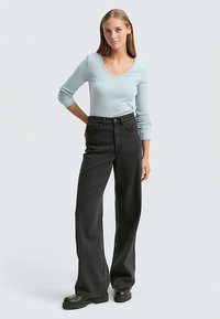 Hellblaues Langarmshirt mit weitem Rundhalsausschnitt, kombiniert mit hoch taillierten schwarzen Weitbein-Jeans. Das Outfit wird durch lässige schwarze Plateau-Schuhe vervollständigt.