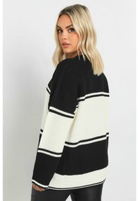 Randig stickad tröja i svart och vitt med lös passform, vida ärmar och ribbat tyg, med kontrasterande horisontella ränder.