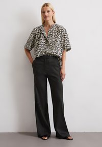 Blouse noire à fleurs à manches courtes avec un col en V, associée à un pantalon noir large taille haute. Tissu lisse avec une coupe ample.