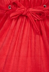 Tejido rojo con un acabado suave y texturizado, que presenta una cintura fruncida y un cinturón atado. Ojales metálicos destacan el cierre con corbata.
