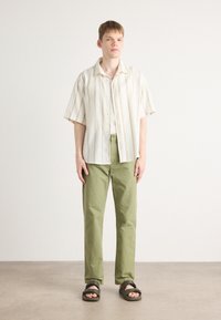 Short-sleeve, collared shirt with cream and yellow stripes, paired with light green trousers and dark sandals. Simple, relaxed fit.