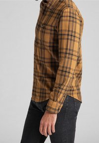 Camicia a quadri marrone con linee nere e arancioni, con bottone nella parte frontale, taschino sul petto, maniche lunghe, realizzata in un tessuto testurizzato.