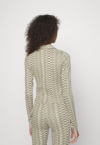 Langärmliger Bodysuit aus einem beige und olivgrün gemusterten Stoff, der eine enge Passform und ein vollständiges Rückendesign mit Logoakzenten aufweist.