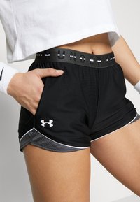 Černé sportovní kraťasy s bílými detaily, s širokým páskem se slogem "UNDER ARMOUR". Materiál vypadá lehce a prodyšně.