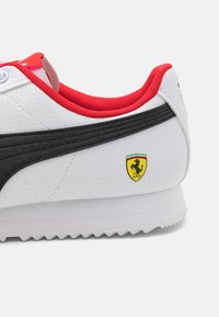 Sneaker bianca con accenti neri. Texture perforata, rifinitura interna rossa e un'emblema giallo Ferrari sul lato. Suola in gomma.