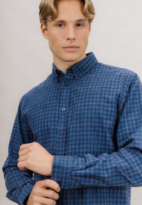 Blå rutete skjorte med knappkrage, med lyse og mørke blåtoner, teksturert stoff og matchende knapper.