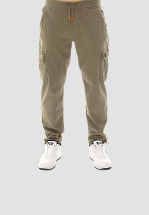 Beige cargobroek met trekkoord in de taille, gedragen met witte sportschoenen op een grijze achtergrond, vooraanzicht van taille tot voeten.