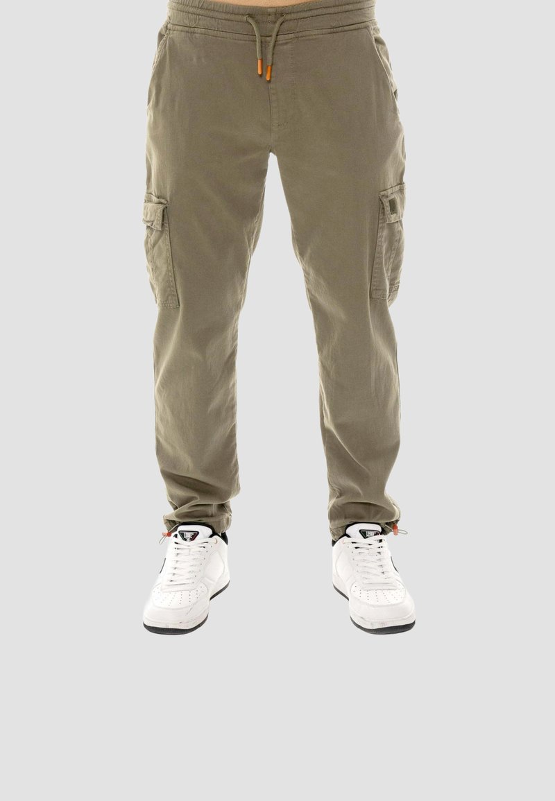 Pantalon cargo beige avec taille à cordon, porté avec des chaussures de sport blanches sur fond gris, vue de face de la taille aux pieds.