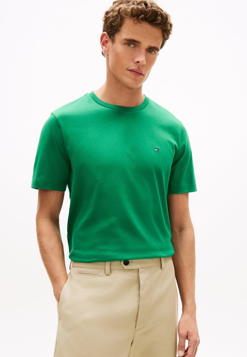 Žalia medvilninė marškinėliai su apvalia iškirpte ir trumpomis rankovėmis, ant krūtinės mažas logotipas. Dėvima su beige spalvos kelnėmis.