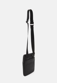 Borsa a tracolla nera in pelle con una texture liscia, forma rettangolare sottile, tracolla regolabile e chiusura superiore con zip.