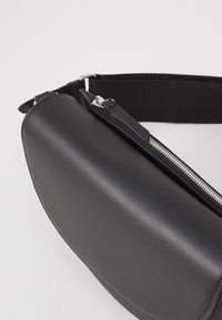 Borsa a spalla in pelle nera con un design elegante e arrotondato, dotata di una cerniera argentata e di una tracolla in tessuto nero. Texture liscia senza motivi.