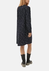 Robe bleu marine avec des motifs floraux blancs et colorés, manches longues, dos froncé, longueur genou, associée à des bottes noires montantes.