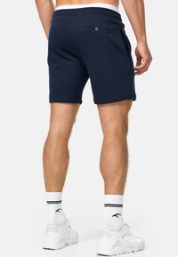 Navyblaue Baumwollshorts mit einer Gesäßtasche, elastischem Bund und seitlichen Schlitzen. Kombiniert mit weißen Socken und Sportschuhen.