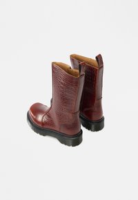 Burgundi krokodilbőr mintázatú bőrbokacsizma lekerekített orral és fekete gumitalppal. Könnyű felvételhez kialakított húzófülekkel.