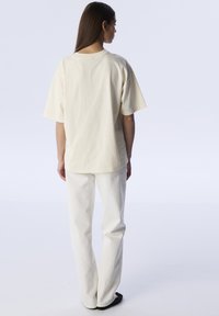 Crème oversized t-shirt van katoen, met korte mouwen en een losse pasvorm, gecombineerd met witte straight-leg broek.