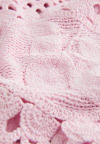 Gros plan d’un tissu crocheté rose doux avec des motifs circulaires et festonnés créant une surface texturée et en relief.