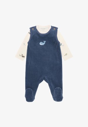 Marineblauw babyrompertje met voetjes en walvisborduursel, gedragen over een crèmekleurig shirt met lange mouwen en kleine walvisprintjes op de mouwen.
