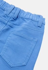 Pantalons en coton bleu clair avec une taille élastique et une poche arrière unique en forme de triangle avec des bords cousus.