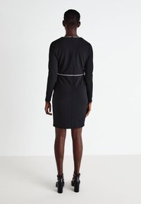 Μαύρο φόρεμα με μακριά μανίκια και κομψή γραμμή, με λευκή λεπτομέρεια στη μέση και φερμουάρ στην πλάτη. Λείος ύφασμα και μήκος μέχρι το γόνατο.