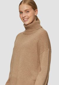 Beige coltrui van zacht breiwerk, met een relaxed fit, geribbelde manchetten en een gladde textuur zonder zichtbare patronen.