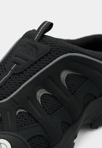 Μαύρο αναπνεύσιμο παπούτσι πεζοπορίας από δίχτυ και καουτσούκ με θηλιά για τράβηγμα και λογότυπο στη γλώσσα, σχεδιασμένο για υπαίθρια χρήση.