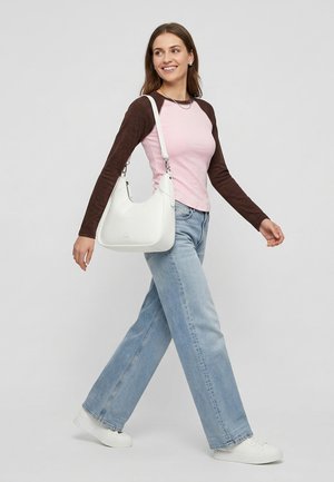 Jeune femme marchant, portant un t-shirt à manches longues rose et marron, un jean bleu clair, des baskets blanches et un sac à bandoulière blanc.