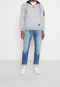 Gray melange pullover hoodie with zip collar and black accents. Paired with light blue denim jeans and white sneakers. Smooth texture.