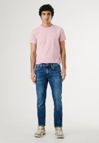 Tricou roz deschis cu mânecă scurtă și guler rotund, purtat cu blugi albaștri din denim și teniși ușori cu talpă groasă.